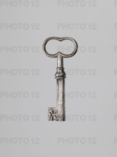 Key, locksmithing. Tubular shaft with a Greek cross cross-section, feather slightly thickened toward the edge. Set in a knot with profiles and a vase element. Oval handle, concave at the knot and at the top. 19th century. Unknown locality. Height 9.6 cm; width 4.1 cm; depth 1.3 cm., A single metallic key suspended against a plain light gray background, showing a rounded double-loop bow with a slightly tarnished silver-gray surface, a slender shaft with a decorative collar near the top, and a rectangular bit at the bottom that has a cutout pattern; overall tones include silver-gray, darker gray areas of wear, and subtle off-white highlights.