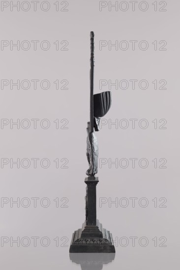 Watch stand with watch, Königlich-Preussische Eisengiesserei in Berlin fl. 1804–1874,  ironworks author or private foundries, watches, eagle iconographic, ca. 1830, Germany, Berlin, varia, height 31 cm, A slender dark metal sculpture stands upright on a tiered rectangular base, with a vertical shaft rising from the base to a thin upper section; a curved, cup-like element projects from one side of the shaft above a textured, elongated form that attaches to the shaft, and the surface shows areas of smoothness and rough, sculpted detail; the overall tones are shades of black and dark gray against a pale gray background, and a soft reflection of the base appears on the glossy surface below.