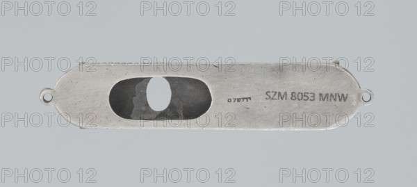 Mezuzah, 19th century, Israel; Judaica; height 0.6 cm, width 6.6 cm, depth 1.3 cm, weight 9 g., A long, narrow metallic object with rounded ends and a central oval opening, showing a darker recessed interior; the metal surface is worn with scratches and small dents; there are a few small circular loops at each end; the overall colors visible are light gray metal, darker gray inside the opening, and a neutral light gray background.