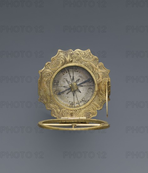 Equatorial sundial by Andreas Vogler ca. 1730–1800, 3rd quarter of the 18th century. Augsburg, Germany. Circular Augsburg-type sundial with a wavy edge; inside the case is a compass with a hinged hour circle and an arched hinged arm marked with geographical latitudes. Engraved decoration on the rim with C-shaped sections and stylized acanthus leaves. Engraved on the underside of the compass case: Eleva. Poli. / Corfu 39 Lyon 45 /' Berlinn 53 Cadiv 36 / Lisabon 39 Paris 48 / Colln 521 Reval 61 / A. Vogler. Function: measuring instrument sundial., An ornate circular metallic object with elaborate scalloped edges and engraved swirling patterns in a golden color, shown open to reveal an inner circular face with a central star-shaped motif and thin dark pointers; the inner face appears silver-gray with aged spots, and the object includes a hinged ring-like component beneath also in gold.