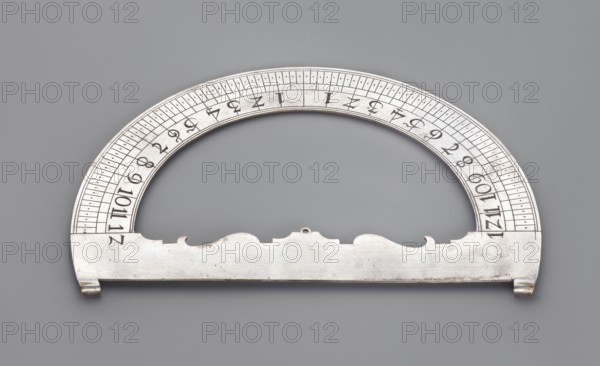 Protractor, acanthus ornament, measuring instrument. Protractor made of silver-plated brass, ca. mid-18th century, Western Europe, height 13.8 cm, width 9 cm., A metallic semicircular instrument rests on a flat background, showing a curved upper arc and a straight lower bar with decorative cutouts along its top edge. The metal surface is silver-gray with areas of slight tarnish and darker spots, and the background is a medium gray. The arc contains a series of evenly spaced short engraved lines and small dots, and the inner arc shows a repeated pattern of short vertical marks. The left and right ends of the straight bar have small hooked projections, and there is a small ring-like loop at the center top of the straight edge. The overall appearance is smooth and slightly reflective, with subtle shadows around the piece.