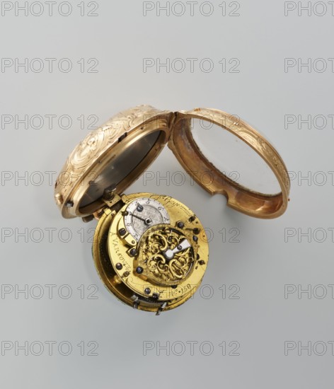 Pocket watch by Franciszek Gugenmus 1740–1820, 2nd half of the 18th century. Gold case depicting symbols of the sciences on a rocaille base; white-enameled dial with Roman and Arabic numerals; openwork hands set with diamonds. Signature on the dial: Fr. Gugenmus / A VASOVIE. On the movement: Fr. Gugenmus / A VARSOVIE / No. 150. Warsaw, Poland. Watch; height 6.5 cm, width 4.5 cm, weight 93.7 g., A partially open ornate pocket watch with its outer case in a warm gold color featuring engraved floral patterns and a hinged glass cover, revealing the inner mechanism that includes a decorative round golden plate with intricate filigree work, visible metal gears and small dark screws, and a smaller silver-toned circular component; the visible colors are gold, silver, dark metallic, and a pale gray background.
