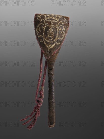 Baroque spoon case with the Korczak coat of arms, coats of arms, Korczak coat of arms, baroque style, leather cover embroidered with metal thread — Korczak coat of arms and SL monogram, tied with crimson cords. Very few cases of this type have been found; this one, along with the spoon for which it was made, is particularly rare. 1st half of the 18th century, Poland, possibly Lviv. Cutlery., An elongated object with a triangular top and a narrow handle, predominantly brown with visible wear and texture, features ornate embroidered decoration in a pale yellowish-gold thread on the triangular section; the edges of that section are trimmed with a faded reddish-pink fabric and there is a braided cord of that same reddish-pink color hanging from the top with frayed ends and knots, while the handle appears darker brown and slightly glossy with signs of age.
