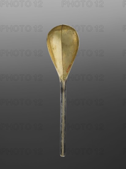 Baroque silver travel spoon with a teardrop-shaped scoop decorated on the reverse with the Korczak coat of arms in a decorative cartouche, flanked by the SL monogram; surrounding decorations of stylized plant twigs; all decorations in niello; the inside of the scoop gilded. Traditional attribution of niello-painted artefacts to the centre in Lviv is not necessarily certain; niello was also used in other centres of the Polish–Lithuanian Commonwealth at that time. Despite the very good quality of the decoration, its value is enhanced by the preserved case, undoubtedly made for it — very few cases without spoons have survived. 1st half 18th century, Poland possibly Lviv. Height 22.9 cm, width 5.6 cm., Korczak coat of arms. Cutlery., A single spoon is shown upright against a gradient gray background, with a teardrop-shaped bowl and a long straight handle; the bowl has a golden color with visible scratches and a few small darker spots, and the handle is darker with metallic tones and a patt...