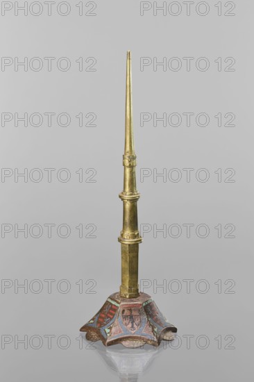 Candlestick, enamel on a hexagonal base tapering towards the top with a shaft; on each side a coat of arms on a blue enamel background eagle and blue lion on horizontal red stripes, between them below the shields on the edges rhombuses with engraved dragons. 19th-century shaft, 14th-century Limoges, Barcelona, lighting, height 32 cm, diameter 11 cm., A tall, slender metallic object with a gold-colored vertical shaft composed of several tapered segments and decorative rings rising from a flared, scalloped base; the base is painted with a pattern showing areas of red, blue, turquoise, and brown, and the surface of the gold shaft shows subtle darker patina and wear.