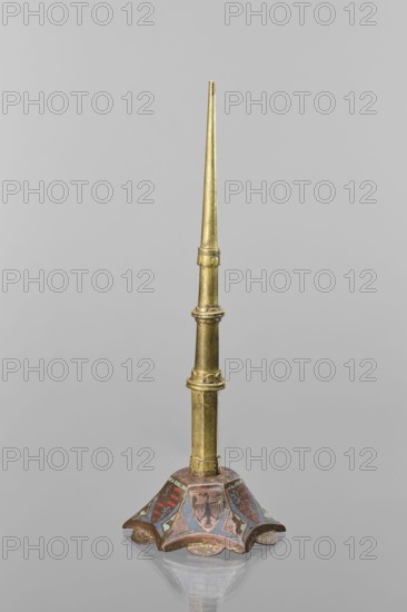 Candlestick, enamel on a hexagonal base tapering towards the top with a shaft; on each side a coat of arms on a blue enamel background eagle and blue lion on horizontal red stripes; between them below the shields on the edges rhombuses with engraved dragons. 19th-century shaft, 14th century Limoges, Barcelona, lighting; height 32 cm, diameter 11 cm., A slender metallic object with a tapered pointed top and a segmented shaft in a golden color stands upright on a decorative base; the base has a flared, scalloped shape with painted panels showing muted colors including red, blue, green, and brown, and the metallic surface shows areas of wear and patina.