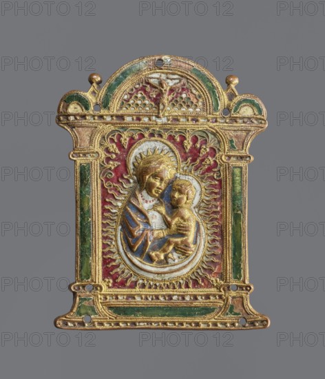 Pax pacific, enamel plaque in the form of a frame with two columns topped by a semicircle; depicts the Virgin Mary and Child, with a depiction of the Crucified in the arch. White, blue, red, and green enamel. 16th century, Spain. Plaque, height 14.5 cm, width 11 cm. Materials: enamel; function: liturgical., A small rectangular metal plaque with an arched top, decorated in relief and surrounded by a raised frame, showing a central oval medallion with two human figures in close embrace; the figures and surrounding ornament are rendered in gilded metal with areas of blue, green, red, and white enamel; the background behind the medallion is red with radiating flame-like motifs in gold; the frame has green enamel panels on the sides and base with gold detailing and small rounded decorative knobs at the top corners; the piece shows textured ornamental patterns, beaded borders, and small drilled holes near the top and bottom edges; the overall color palette includes gold, green, red, blue, wh...
