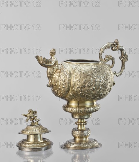 Water tincture, Schweiger, Matthias fl. ca. 1623–1635 goldsmith; herms decorative elements; lions; flowers ornament; fruit ornament; acanthus ornament. Jug with a spherical belly decorated with repoussé bouquets of flowers and fruit in acanthus reserves; on the side a spout in the shape of a female half-figure holding a conch; on the axis a plastic handle formed of channel sections connected by a winged herm of a woman. The cover is topped with a plastic lion standing on its hind legs. 1630–1635, Augsburg, Germany. Vessel; height 28 cm, width 14 cm, depth 30 cm., A decorative metallic vessel and its separate lid sit against a plain light gray background, both items displaying ornate embossed and chased patterns with scrollwork and floral motifs; the vessel has a rounded body on an embellished stem and foot, a curved decorative handle with scroll and acanthus designs, and a sculpted spout featuring a small human-like figure holding a shell-shaped element, while the lid shows a standing ...