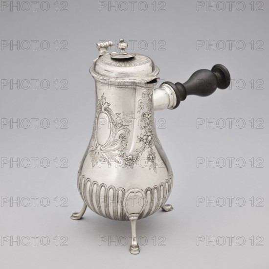 Chocolate jug by Edme-Pierre Balzac fl. 1739–1781, goldsmith. Pear-shaped chocolate vessel supported on three legs, with a small spout and a hinged lid; circular opening with a sliding circular lid. Lower belly decorated with vertical curls; upper part with repoussé garlands and an oval reserve. Dated 1764–1765, Paris, France. Dimensions: height 26 cm, width 24 cm, depth 13.5 cm. Purchased in 1883 as vieux Paris for 500 francs., A silver metal pitcher with a rounded, bulbous body standing on three curved feet, featuring engraved floral garlands and ornamental cartouches on its polished surface, a hinged domed lid with a small finial and decorative ridging, and a dark wooden side handle attached to a short metal socket; the visible colors are silver, dark brown, and gray.