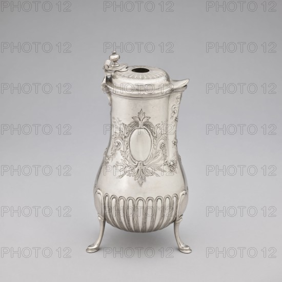Chocolate jug by Edme-Pierre Balzac fl. 1739–1781, goldsmith. Pear-shaped chocolate jug supported on three legs, with a small spout and a hinged lid featuring a circular opening and a sliding circular lid. The lower part of the belly is decorated with vertical curls; the upper part with repoussé garlands and an oval reserve. France, Paris, 1764–1765. Vessel; height 26 cm, width 24 cm, depth 13.5 cm., A single metal pitcher with a hinged lid and a short spout stands on a neutral light gray background; the pitcher is silver in color with a polished finish and rests on a group of three curved legs, its body narrowing at the top and widening toward a rounded base decorated with a series of vertical fluted ridges, and the upper body features ornate embossed floral and foliate motifs surrounding an oval cartouche, while the lid has a ribbed design and a small finial with a hinge decorated by a curled element.
