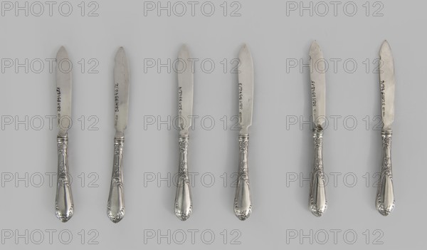 6 fruit knives; maker: Adam Nagalski 1862–1944, goldsmith; dated 1915–1920; Warsaw, Poland; cutlery; dimensions: height 17.3 cm, width 1.8 cm., A row of several metal knives arranged horizontally against a light gray background, each knife showing a shiny silver blade and an ornate silver handle with floral and scrollwork decoration; the handles have reflective surfaces and curved teardrop-shaped ends, while the blades have a matte silver appearance with slight variations in wear and small dark marks.