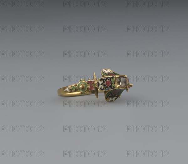 women's ring, 19th century, Poland, jewelry, height 2.4 cm, width 2.1 cm, A gold ring with ornate enamel decoration rests on a neutral gray surface against a darker gray background. The ring features a central bezel set element with a faceted stone and surrounding decorative panels shaped like petals or wings, decorated with enamel in green, red, white, and black. The band shows additional enamel ornamentation in green and red on a gold base. The overall colors visible are gold, green, red, white, black, and gray.