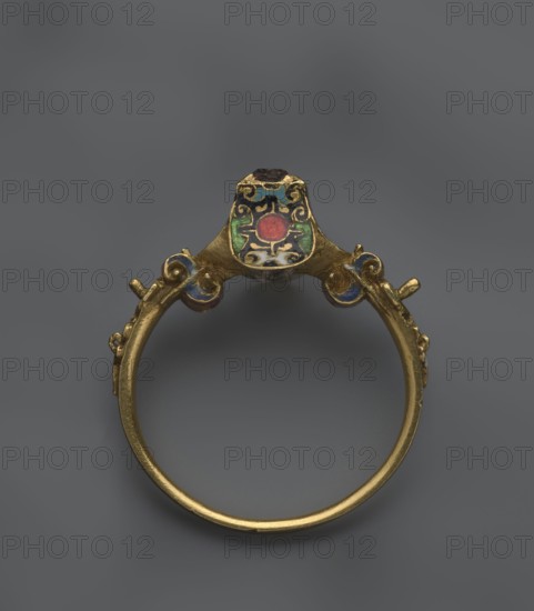 Women's ring, 19th century, Poland; jewelry; height 2.4 cm, width 2.1 cm, A gold ring viewed from above with a rounded band and an ornate top section featuring cloisonné enamel in colors including red, green, blue, black, white, and gold; the top has a central red circular enamel surrounded by green and blue panels and black scroll-like patterns, and the band shows small decorative protrusions and curled elements that are also accented with blue enamel, all set against a uniform gray background.