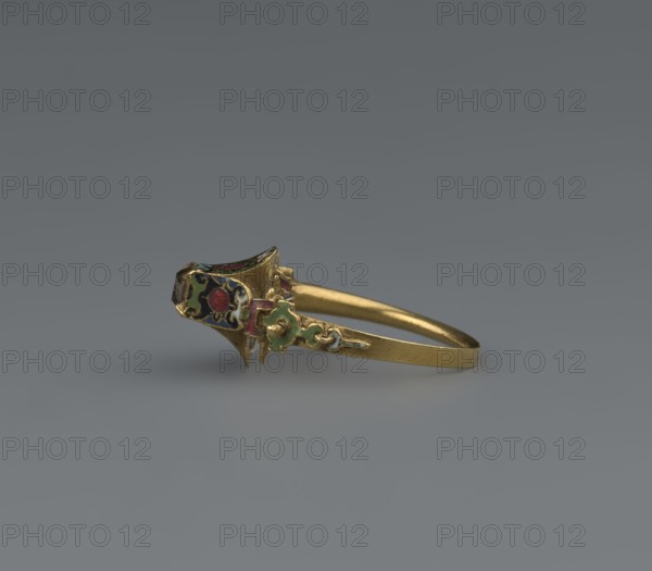 Women's ring, 19th century, Poland; jewelry; height 2.4 cm, width 2.1 cm, A gold ring resting on a smooth gray surface, featuring an ornate decorative head with cloisonné-like enamel inlays in red, green, black, and white, and a slender plain gold band extending from the decorated section.