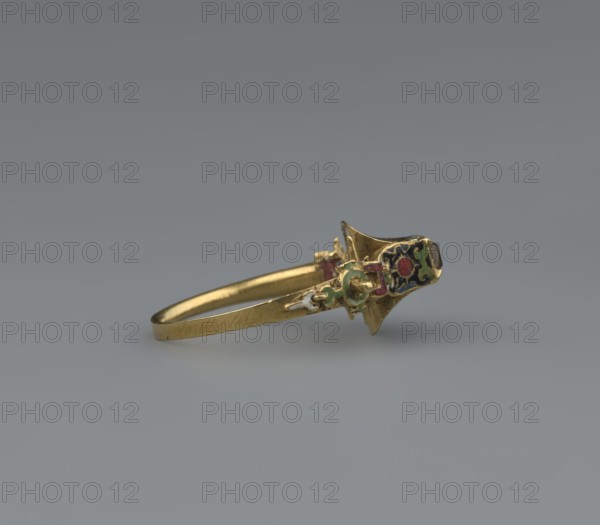 women's ring, 19th century, Poland, jewelry, height 2.4 cm, width 2.1 cm, A close-up of a gold ring lying on a smooth gray surface, featuring an ornate setting with small areas of colored enamel in green, red, blue, white, and black on the decorative top; the band is thin and gold with a slightly worn texture, and the background is a uniform gray gradient.