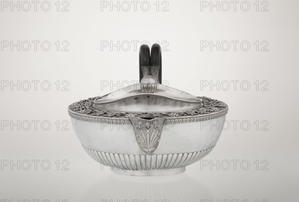 Teapot, Rundell Bridge & Rundell fl. ca. 1788–1845 with maker's firm Scott, Digby & Smith, Benjamin fl. 1802–1807; vines, snake iconography; Pogon Ruska coat of arms; tea vessel; coats of arms; rank crowns; princely mitre heraldry; mottos heraldry; paludamentum heraldry; acanthus leaves ornament; clasp; labry heraldry. Hemispherical, on a low cylindrical pedestal; body decorated in the lower part with radial curls and at the upper edge with a band of acanthus leaves; hinged lid surrounded by a raised collar with an applied vine branch with clusters; double handle of blackened wood set in caps upper caps shaped as snake heads, lower as tails. Czartoryski coat of arms applied on a paludament with labry and the motto Badz co sie jest. 1803–1804, London, England. Vessel; height 13 cm, width 24.6 cm, depth 17.2 cm, weight 1002 g., A silver bowl with a decorative lid and a dark handle behind it sits centered on a pale background; the bowl shows a band of vertical fluting near its base and a ...