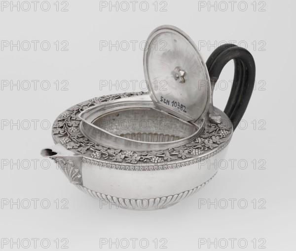 Teapot, Rundell Bridge & Rundell fl. ca. 1788–1845 goldsmith's firm; Scott, Digby & Smith, Benjamin fl. 1802–1807 goldsmith; vines, snake iconography; Pogon Ruska coat of arms; purchase provenance; tea vessel; coats of arms; tea vessel; rank crowns; princely mitre / heraldry; mottos heraldry; paludamentum heraldry; acanthus leaves ornament; clasp; labry heraldry. Hemispherical, on a low cylindrical pedestal, with a body decorated in the lower part with radial curls, at the upper edge with a band of acanthus leaves; a hinged lid surrounded by a raised collar with an applied vine branch with clusters; a double handle made of blackened wood, set in caps the upper ones in the shape of snake heads, the lower ones in the shape of tails; the Czartoryski coat of arms applied on a paludament with labry and the motto Badz co sie jest. 1803–1804, London, England. Vessel; height 13 cm, width 24.6 cm, depth 17.2 cm, weight 1002 g., A decorative metal vessel with an open hinged lid sits on a light b...