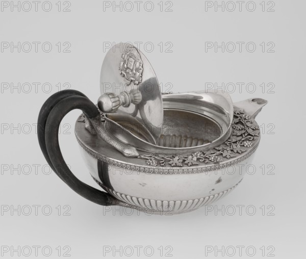 Teapot, Rundell Bridge & Rundell fl. ca. 1788–1845 goldsmiths, Scott, Digby & Smith, Benjamin fl. 1802–1807 goldsmiths; tea vessel, 1803/1804, London, England. Hemispherical vessel on a low cylindrical pedestal; body decorated in lower part with radial curls and at the upper edge with a band of acanthus leaves; hinged lid with raised collar bearing an applied vine branch with clusters; double handle of blackened wood set in caps upper caps shaped as snake heads, lower as tails. Applied Czartoryski coat of arms on a paludament with labry and the motto Badz co sie jest; motifs include vines, snake, Pogon Ruska coat of arms, rank crowns, princely mitre, mottos, paludamentum, acanthus leaves, clasp, labry. Tea vessel; height 13 cm, width 24.6 cm, depth 17.2 cm, weight 1002 g., A silver bowl-like vessel with an open hinged lid sits against a light gray background, showing a dark curved handle attached to one side. The vessel has a rounded body with fluted lower decoration and an ornate rim ...