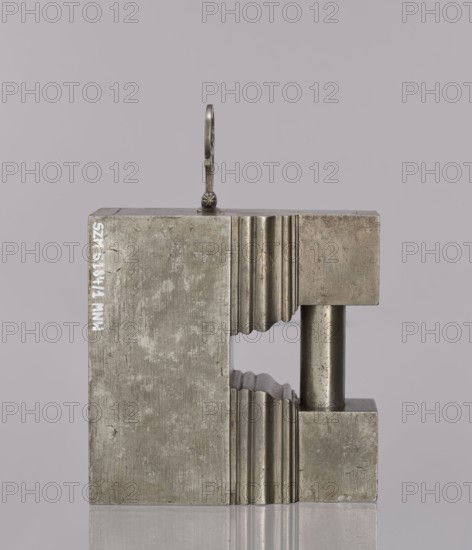 Padlock, 19th century. A padlock in the shape of a cuboid with the upper part topped by a cornice; on each side two small cuboids are connected by a cylindrical rod functioning as an earring. After unlocking, the side wall together with the earring is pulled out, facilitated by an openwork hinged handle. The keyhole is horizontal on the longer wall. Technique: locksmithing. Dimensions: height 12.6 cm, width 12.7 cm, depth 6.2 cm., A metal block with a rectangular shape and a U-shaped cutout sits upright against a pale gray background; the block has a rough, weathered surface in metallic gray and shows a few vertical ridged patterns on the inner faces of the cutout, a cylindrical metal rod of darker gray spans the gap on one side, and a small metal loop with a decorative knob is attached to the top.