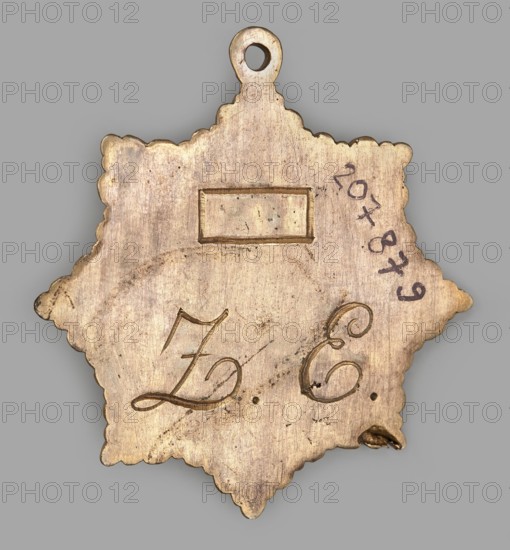 Badge of the lodge zur Einigkeit, Gdansk, freemasonry, masonic lodge insignia. Eight-pointed radiant star with a central triangle containing an enameled circle surmounted by a cross. In the circle, on a purple background, two hands holding a laurel wreath; in the triangle above, the Eye of Providence within rays. Reverse bears lodge initials ZE. Ring for hanging on a ribbon attached. Circa 1880, Poland. Height 5.8 cm, width 5.5 cm., A star-shaped metal pendant with scalloped edges and a small circular loop at the top, shown against a gray background. The pendant has a worn, metallic surface in tones of dull gold and brass with areas of darker tarnish and spots of discoloration. There is a rectangular recessed panel near the top and a few engraved curving decorative marks toward the center and lower right. The metal shows scratches, small pits, and an irregular dent or bend near the lower right edge.