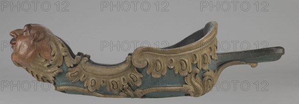 Sleigh, rococo two-seater, carved, polychrome, gilded; 3rd quarter of the 18th century, Poland . Sleigh in the shape of a gondola made using the dugout canoe method, painted blue, with a wavy upper rim highlighted by a half-cylinder and channel sections with rocaille motifs; front in the form of a mascaron painted red, framed with acanthus leaves; rear trestle originally upholstered with carved acanthus underneath; inside the sleds four sockets for connection with skid supports; mascarons, men's heads, rocaille and acanthus ornamentation; height 57 cm, width 208 cm, depth 68 cm., A carved decorative object resembling a boat-like form with a sculpted human head at one end, showing skin tones of reddish-brown and darker brown, and hair carved in a muted gold color; the main body is painted a muted teal or blue-green with ornate carved scrollwork and leaf motifs in shades of gold and beige, and the interior appears darker, near black or deep brown; there are areas of worn dark brown wood ...
