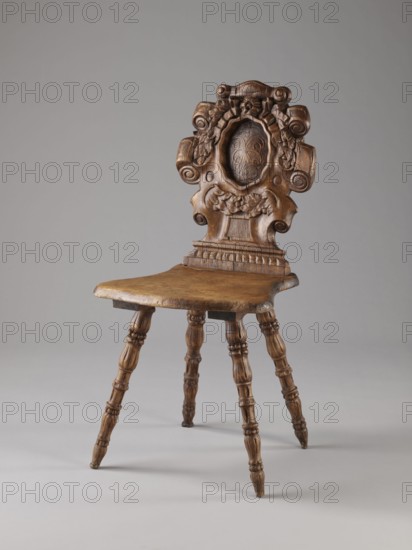 Stool, ca. 1850, possibly Warsaw; neo-Renaissance style; piece of furniture — seating; height 90 cm, width 44 cm, depth 45 cm; materials/ornament: scrollwork, cabochon., A wooden chair with a carved backrest featuring ornate scrolls and floral motifs and a central oval medallion, a contoured wooden seat with a smooth worn surface, and a group of turned wooden legs with spindle-like detailing; the visible colors are various shades of brown in the wood and a neutral gray background.