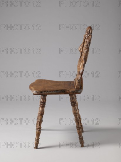 Stool, ca. 1850, possibly Warsaw; neo-Renaissance style; scrollwork and cabochon ornament; piece of furniture — seating piece; height 90 cm, width 44 cm, depth 45 cm., A wooden chair shown from the side with a carved backrest and a flat seat, both in brown wood tones; the backrest features carved decorative shapes and a textured surface, and the seat edge appears worn. The chair has a set of turned legs with carved rings and rounded sections, matching the brown color of the seat and back. The background is a smooth light gray and the floor area is a slightly darker gray, with soft shadows beneath the chair. The visible colors are brown and gray.
