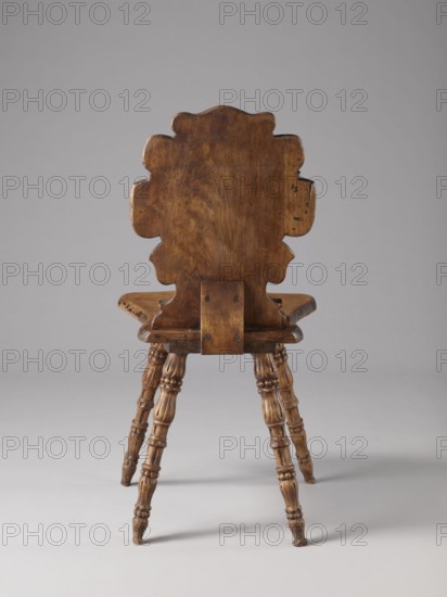 Stool, ca. 1850, Warsaw, neo-Renaissance style, scrollwork and cabochon ornament, wooden seating piece, height 90 cm, width 44 cm, depth 45 cm., A wooden chair viewed from the back with a carved scalloped backrest and a curved seat, showing the wood grain and a warm brown finish; the backrest has a rectangular support plate attached with visible fasteners and slightly irregular edges; the chair stands on a group of turned, carved legs with rounded and fluted details, all in similar brown tones; the background is a smooth neutral gray and the floor area beneath the chair is a lighter gray.
