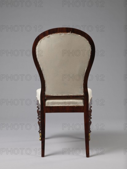 Chair with a padded balloon backrest and a trapezoidal padded seat removable cushion. Front legs are spool-turned, on brass rollers with clamps; rear legs are angular, tapered, slightly arched backwards, continuing into the backrest frames. Low frame with rounded front corners. Upholstery fabric not original: damask with a large floral pattern in purple and cream, finished with upholstery tape. Circa 1840, Warsaw. Seating furniture; height 97.5 cm, width 48 cm, depth 53.7 cm., A wooden chair shown from the back with a curved top rail and an exposed upholstered back panel in an off-white fabric with frayed edges, the wood showing a dark brown finish with visible grain, a cushioned seat covered in the same off-white fabric, turned front legs in dark brown with small brass casters and straight rear legs, all set against a neutral gray background; visible colors include off-white, dark brown, brass, and gray.