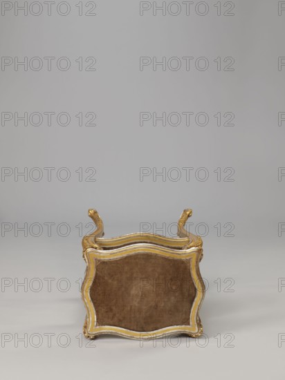 Side table, equipment of representative buildings of the Republic of Poland 1918–1939, plant decoration with acanthus ornament and volutes, neo-rococo style, 3rd quarter of the 19th century, Warsaw; furniture, table; height 77.3 cm, width 50 cm, depth 40 cm, A small ornate stool or low seat is shown from the top edge, with a curved, scalloped wooden frame finished in gold and a muted white trim surrounding a velvet-like upholstered panel in a warm brown tone; the frame has decorative carved handles that curve upward at opposite sides and show gold highlights, and the background and floor are smooth, even shades of light gray.