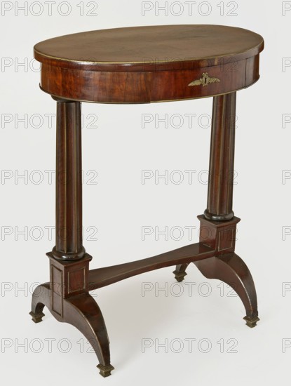 Table, Empire style, columns, floral decoration. Oval-top table with a drawer in the frame, supported by two supports in the form of fluted columns on bipods, fastened at the bottom with a board link. Supports taper upwards, with turned bases and disc-shaped heads, mounted on plinths from which arise arched, tapering legs with cast brass profiled feet. Link is narrowed in the middle. Edges—the top of the top, the bottom of the frame, the top of the links and bipods, and the ridges of the flutes—are banded with semicircular brass strips; frames on the faces of the blocks made of brass strips. Drawer lock is a single-bolt steel mortise lock with a medallion-shaped plate with a bow at the top and two branches at the bottom. Dated 1815–1825, Central Europe. Furniture, table. Dimensions: height 79 cm, width 62.5 cm, depth 47 cm., A small oval wooden table with a polished brown top and rounded edge, supported by two turned vertical wooden columns that connect to a horizontal stretcher; the a...