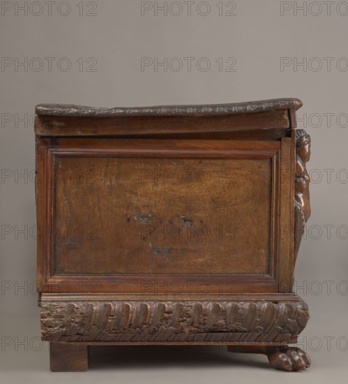 Chest, acanthus twig, fantastic animals, fantastic figures, snakes, coats of arms, herms decorative element, Renaissance style, animal paws, walnut. Cuboid carved chest supported by four low legs, the front ones shaped as lion's paws, the rear ones angular. Front has an applied profiled frame enclosing a pseudo-panel carved with grotesque elements on a grained background: central section shows two winged genii merging at the bottom into an acanthus twig, holding a laurel wreath above a scrollwork cartouche framing the lock; between the volutes are twigs, snakes and griffins. Herms in the front corners. Prominent plinth molding symmetrically decorated with gadroons. Straight side walls, originally with doorknobs. Interior on the left side of the cabinets. Hinges and lock striker of tinned, engraved steel. Ca. mid-16th century, Italy. Piece of furniture, storage unit. Height 54.5 cm, width 165.2 cm, depth 57 cm., A wooden chest with a rich brown finish is shown against a neutral gray bac...