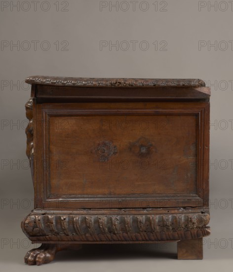 Chest, acanthus twig, fantastic animals, fantastic figures, snakes, coats of arms, herms decorative element, Renaissance style, animal paws, walnut. Cuboid carved chest supported by four low legs, front ones shaped as lion's paws, rear ones angular. Front with an applied profiled frame enclosing a pseudo-panel carved with grotesque elements on a grained background: central section with two winged genii merging at the bottom into an acanthus twig, holding a laurel wreath above a scrollwork cartouche framing the lock; between the volutes, twigs, snakes and griffins. Herms at the front corners. Prominent plinth molding symmetrically decorated with gadroons. Straight side walls, originally with doorknobs. Interior on the left side of the cabinets. Hinges and lock striker of tinned, engraved steel. Circa mid-16th century, Italy. Piece of furniture, storage unit. Height 54.5 cm, width 165.2 cm, depth 57 cm., The image shows a wooden piece of furniture photographed from the side, with a brown...