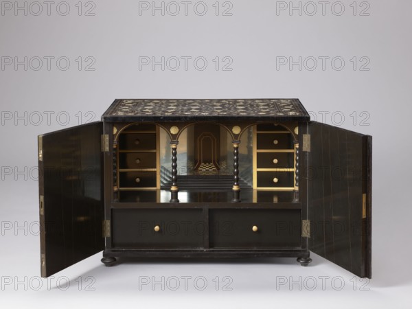 Cabinet, plant decoration, columns architectural, rosettes ornament, early 20th century, India possible origin, Europe possible origin, piece of furniture, storage piece; height 46.2 cm, width 63 cm, depth 43 cm., A small black wooden cabinet with its two side doors open, revealing an interior divided by three arched openings supported by three twisted columns; the top surface of the cabinet has ornate inlaid decoration in lighter tones. Inside the cabinet, there are a few small drawers on each side with round knobs and painted gold-colored edges, and two larger drawers at the bottom with similar round knobs. The arches and column capitals show gold-colored decorative details, and the back interior features a painted scene with a checkered floor pattern and architectural elements in muted blues and browns. The cabinet rests on short bun feet and is shown against a light gray background; visible colors include black, gold, brown, blue, and gray.