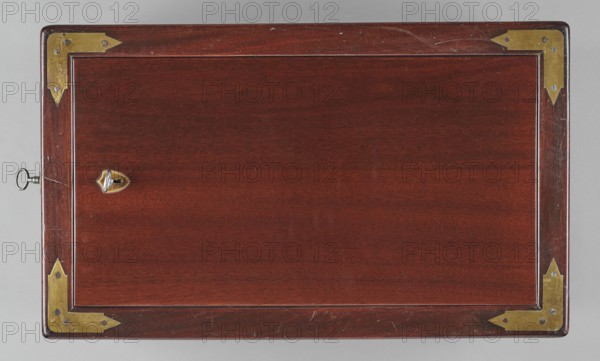 Bidet, unknown origin, hygiene; cuboid mahogany bidet containing a plated container of the same shape, closed with a removable lid; with folding supports. Hinged supports on the shorter sides with an S-shaped outline, forming a rectangular plate when folded the wider support on the inside is cut in the form of a concave–convex arch, filled with a narrower one of the same outline. Frame cover with a single removable panel. Brass fittings: strip fittings in the corners of the body three each and the lid single, sapphire hinges; a latch locking the supports, folding rotating locks for both supports, and a pair of flat locks for the rear support. Removable container with extendable handles made of thick wire. 18th/19th century, England; furniture, toilet equipment; height 52.2 cm, width 47.7 cm, depth 28.5 cm., A rectangular wooden box top viewed from above with a polished dark reddish-brown surface and a narrow raised inner border; each corner has a brass corner plate with visible screws ...