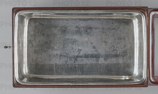 Bidet, unknown origin, hygiene, cuboid mahogany bidet containing a plated container of the same shape, closed with a removable lid; with folding supports. Hinged supports placed on the shorter sides with an S-shaped outline, forming a rectangular plate when folded the wider support on the inside is cut in the form of a concave-convex arch, filled with a narrower one of the same outline. Frame cover with a single removable panel. Brass fittings: strip fittings in the corners of the body three each and the lid single, sapphire hinges; a latch locking the supports, folding, rotating locks for both supports, and a pair of flat locks for the rear support. Removable container with extendable handles made of thick wire on the long sides. 18th/19th century, England, furniture, toilet equipment. Height 52.2 cm, width 47.7 cm, depth 28.5 cm., A rectangular metal tray with rounded inner corners set into a wooden frame, showing a worn and scratched reflective surface with patches of darker tarnish...