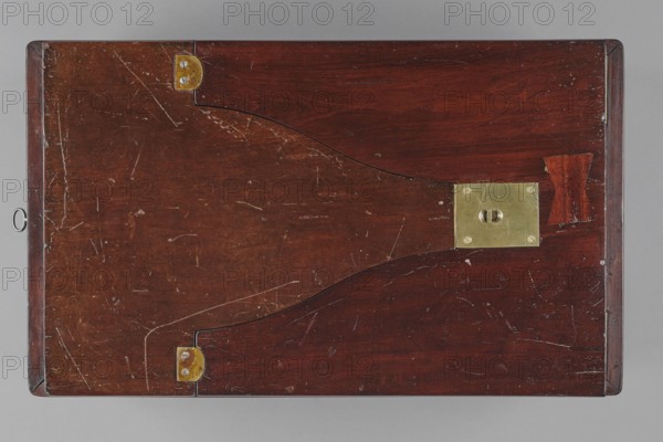 Bidet, unknown origin, hygiene; cuboid mahogany bidet containing a plated container of the same shape, closed with a removable lid; with folding supports. Hinged supports placed on the shorter sides with an S-shaped outline, forming a rectangular plate when folded the wider support on the inside is cut in the form of a concave-convex arch, filled with a narrower one of the same outline. Frame cover with a single removable panel. Brass fittings: strip fittings in the corners of the body three each and the lid single, sapphire hinges; a latch locking the supports, folding, rotating locks for both supports, and a pair of flat locks for the rear support. Removable container with extendable handles made of thick wire. 18th/19th century, England; furniture, toilet equipment; height 52.2 cm, width 47.7 cm, depth 28.5 cm., A flat rectangular wooden surface with a reddish-brown finish showing grain and many light scratches and scuffs, edged by slightly darker wooden borders, a few brass fitting...
