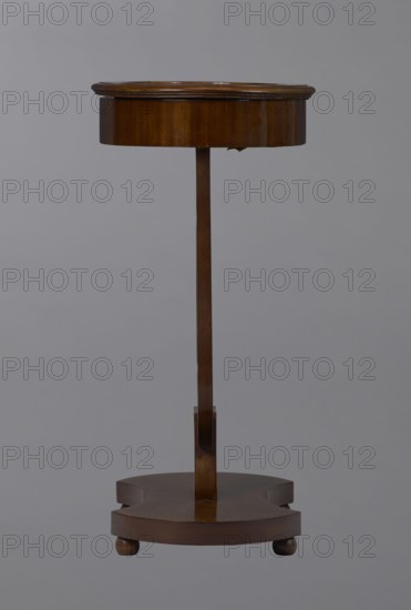 Oval display table with a lyre-shaped base mounted on a platform with a concave-convex outline, supported by four spherical legs. Veneered in mahogany. Lyre strings terminate at the top with balls. The edge of the tabletop frame is profiled. 1820–1840, Central Europe. Piece of furniture for displaying objects. Height 76.7 cm, width 52.3 cm, depth 37.9 cm., A wooden pedestal table with a round top and a slender central column rising from a shaped circular base, the wood showing warm brown tones and a polished finish, the top having a slightly raised edge and the base standing on a few short rounded feet against a plain gray background.