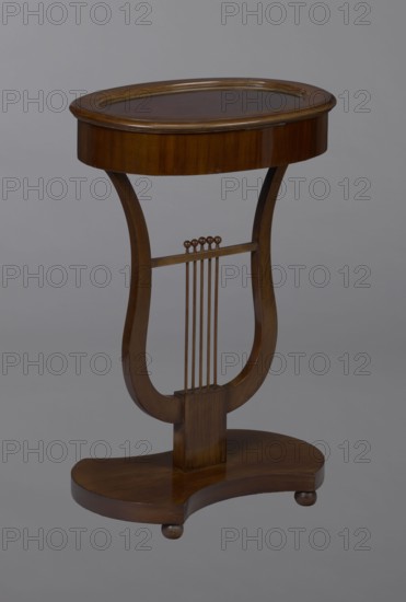 Oval display table with a lyre-shaped base mounted on a platform with a concave-convex outline, supported by four spherical legs. Entirely veneered with mahogany. Lyre strings terminate at the top with balls. The edge of the tabletop frame is profiled. Lyres musical instrument motif. Piece of furniture for displaying objects., Date: 1820–1840. Central Europe. Height 76.7 cm; width 52.3 cm; depth 37.9 cm., A wooden small table with a rounded oval top supported by a lyre-shaped central column that connects to a curved base; the wood shows warm brown tones with lighter and darker grain variations, and there are a few small rounded wooden knobs and thin vertical wooden rods in the central section, all set against a neutral gray background.