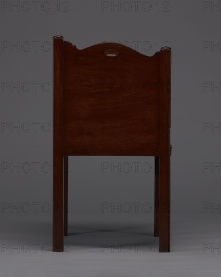 Bedside table with toilet, 4th quarter of the 18th century, England. Bedstand with toilet, with a tambour door in the upper section and a pull-out section below with a circular opening for a bedside chamber pot with a lid. Supported by four angular stand-up legs; the front legs divided diagonally in half, the front half connected to the front, wavy-cut board of the pull-out section at the bottom. Pull-out handle of gilded brass. The opening cover is turned, recessed in the center, with a round handle. Front and side walls of the body have wavy-cut tops with oval openings as handles. A blind consisting of two parts that slide sideways, with small brass knobs. A piece of furniture for hygiene. Height 82 cm, width 59.2 cm, depth 45 cm., A wooden chair seen from the back with a dark reddish-brown finish, straight square legs, and a rectangular back panel topped with a gently curved crest that has a small oval cutout; the background is a uniform mid-gray and the floor is a lighter gray, wit...