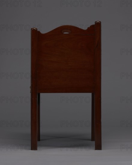 Bedside table with toilet, 4th quarter of the 18th century, England. Bedstand with toilet, with a tambour door in the upper section and a pull-out section below with a circular opening for a bedside chamber pot with a lid. Supported by four angular stand-up legs; the front legs divided diagonally in half, the front half connected to the front wavy-cut board of the pull-out section at the bottom. Pull-out handle of gilded brass. Opening cover turned, recessed in the center, with a round handle. Front and side walls of the body have wavy-cut tops with oval openings as handles. A blind consisting of two parts that slide sideways, with small brass knobs. Function: piece of furniture for hygiene. Dimensions: height 82 cm, width 59.2 cm, depth 45 cm., A wooden chair viewed from the back, showing a tall rectangular back panel with a gently curved top rail and a small oval cutout near the top; the chair has straight, square legs and a smooth wood grain surface. Visible colors include dark brow...