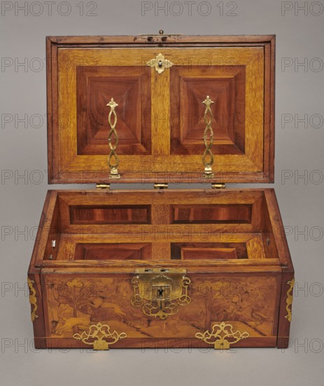 Casket, Baroque cuboid case inlaid with figural scenes and openwork brass fittings. Front shows a deer hunt with dogs; lid has an oval scene of a sleigh drawn by a deer. Interior: beneath the chamber bottom are three drawers middle smaller accessible after folding down the front wall. Lid contains a compartment closed with a plate on brass hinges. Fittings cut from thick brass sheet on lid edges and body corners. Bottom and back wall fastened with strap hinges with decorative openwork finials visible from back of lid and at bottom of front wall. Mortice-type lock with two catches mounted on bottom of lid. Dated 1720–1740, Germany. Furniture — storage furniture. Dimensions: H 21.6 cm, W 42.5 cm, D 27.4 cm., An open wooden box with a hinged lid reveals an interior and exterior of polished wood in warm brown and golden tones, the lid and inner panels featuring geometric recessed rectangles and squares, and the front and sides decorated with engraved scenes of animals and trees in darker b...