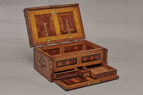Casket, Repossession noted. Cuboid case inlaid with figural scenes and openwork brass fittings. Front shows a deer hunt with dogs; lid has an oval field depicting a sleigh drawn by a deer. Inside, beneath the chamber floor, are three drawers middle smaller accessible after folding down the front wall. Lid contains a compartment closed with a plate on brass hinges. Fittings cut from thick brass sheet on lid edges and body corners. Bottom and back wall fastened with strap hinges with decorative openwork finials visible from the back of the lid and at the bottom of the front wall. Mortice-type lock with two catches mounted on the bottom of the lid. Baroque style, 1720–1740, Germany. Furniture — storage furniture. Dimensions: height 21.6 cm, width 42.5 cm, depth 27.4 cm., A wooden chest sits open on a neutral gray surface, showing an interior of polished wood panels in warm brown and reddish-brown tones with lighter golden-brown trim; the raised lid displays geometric paneling and brass de...