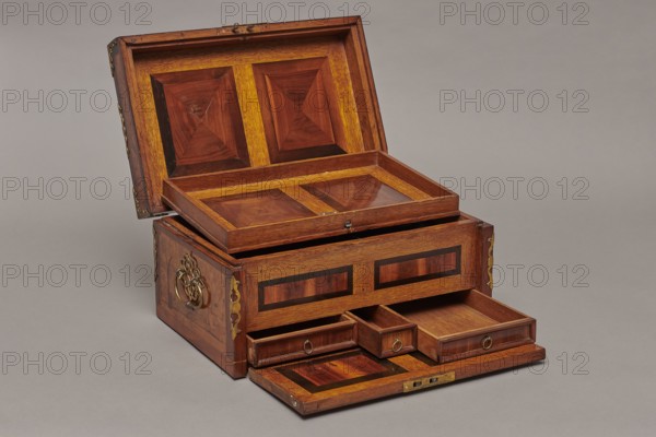 Casket, repossession provenance. Sleigh, deer, hunters, hounds, riders; Baroque style. Cuboid case inlaid with figural scenes and fitted with openwork brass fittings. Front of the body shows a deer hunt with dogs; lid bears an oval field depicting a sleigh drawn by a deer. Interior: beneath the chamber floor are three drawers middle smaller accessible after folding down the front wall. Lid contains a compartment closed with a plate on brass hinges. Fittings cut from thick brass sheet on lid edges and body corners. Bottom and back wall fastened with strap hinges with decorative openwork finials visible from the back of the lid and at the bottom of the front wall. Mortice-type lock with two catches mounted on the bottom of the lid. Date: 1720–1740. Place of origin: Germany. Furniture — storage furniture. Dimensions: H 21.6 cm, W 42.5 cm, D 27.4 cm., An open wooden chest with a hinged lid revealing an inner tray and several pull-out compartments, all showing wood grain in warm brown and r...