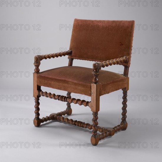 Armchair, Baroque;, circa 1640–1660, France. Upholstered seat and backrest with cherry plush covering the frame and backrest rails, finished with upholstery tape at the bottom of the backrest. Spirally turned frame elements and carved armrest supports; armrest supports low, in the form of female busts mounted on turned balusters. Wide rectangular seat and slightly reclined backrest with clearance and turned side rails in the lower part. Seat with secondary upholstery on springs. Legs end with glides-pads, joined by an H lacing at the bottom; front legs additionally fastened with a high link; joints of the footrest elements form ankles and the upper part of the front legs is elongated. Seating piece armchair. Dimensions: height 84.5 cm, width 61 cm, depth 51 cm., A wooden armchair with a fabric upholstered seat and back, featuring twisted turned legs and stretchers, carved arm supports, and a warm brown upholstery; the wood shows tones of medium to dark brown and the fabric appears rust...