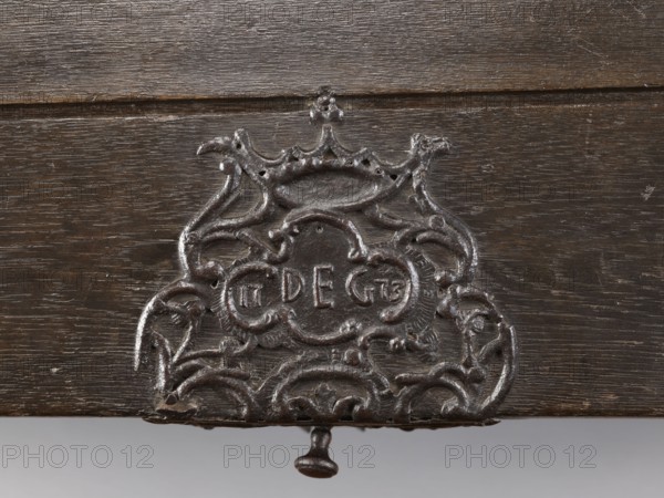 Chest, provenance, dowry chest with convex lid and side walls slightly tapering toward the bottom; richly decorated with openwork repoussé fittings featuring plant motifs, rocaille and stylized acanthus ornamentation, rococo and baroque stylistic elements, crowns and monograms. On the front of the lid, on the axis, an openwork plate with a rococo cartouche contains the date and initials 17 DEG 73. The lid sides have two decorative strap hinges extending into the front decoration, where fittings form a horizontal composition of five asymmetrical cartouches decreasing toward the sides. Side edges of the lid are edged with openwork bands; analogous openwork applications are in the body corners. Side walls feature large openwork plates; lid boards are joined with tongue-and-groove joints. 2nd half of the 18th century 1773?, Central Europe; piece of furniture/storage unit. Dimensions: height 69.7 cm, width 129.4 cm, depth 63.5 cm., A close-up view of a dark brown wooden surface with a weath...