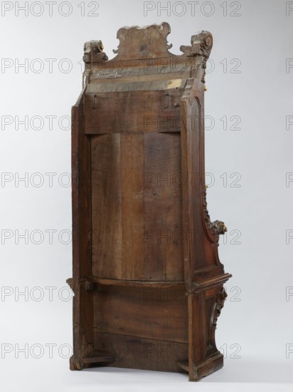 Church throne armchair, carved, mid-18th century, Italy. Seating piece; height 201.5 cm, width 81 cm, depth 59 cm. High rectangular backrest in the form of an aedicula topped with a volute top; supported on a platform cut out in the shape of the letter U. Two console supports for the board seat; supports, sides, and lower part of the back with a frame structure. Seat with concave outline, profiled rim, lifting in the middle on hinges. Aedicula backrest made of two parts, with a shell at the top framed by a profiled cornice. Lower side walls arch into the armrests. Upper part of the seat supports, armrests, and side pinnacles carved with volutes formed of acanthus leaves. Aedicule shell rim and finial volutes gilded. Baroque style; ornament: shells, acanthus, volutes; function: church furnishings., A tall wooden furniture piece shown from its back with visible wood grain and signs of wear, featuring a carved crest at the top and carved scroll-like ornaments on the upper sides, a recesse...