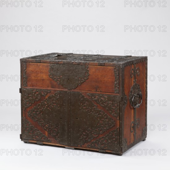 Cabinet, pre-war, grotesques ornament, fantastic animals, Hermes mythology, male figures, wickerwork ornament, fantastic figures, plant tendril. Cuboid cabinet with a drawer at the top and double doors below, richly decorated with openwork engraved fittings with grotesque motifs. The door leaves are veneered on the inside with rosewood and ebony in geometric arrangements, divided by inlaid bone vein, with figures in engraved bone, signed—Hippocrates on the left, Hermes on the right. Behind the doors are twelve compartments. Steel plate fitted for drawer and door locks; the drawer lock blocks the left door leaf. Steel hinges. Late 17th century, Northern Germany, Poland . Piece of furniture, storage piece. Height 70.1 cm; width 89.2 cm; depth 55.9 cm., A wooden chest with a warm brown finish sits against a pale background, featuring dark metal decorative plates and hardware across its front, top, and sides; the metalwork has ornate, filigree-like patterns and scalloped edges, including a...