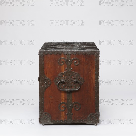 Cabinet, late 17th century, Northern Germany, / Poland, height 70.1 cm, width 89.2 cm, depth 55.9 cm. Cuboid cabinet with a drawer at the top and double doors below, richly decorated with openwork engraved fittings with grotesque motifs and fantastic animals. Door leaves veneered on the inside with rosewood and ebony in geometric arrangements, divided by inlaid bone veining, with figures in engraved bone: signed Hippocrates on the left and Hermes on the right. Behind the doors are twelve compartments. Drawer and door locks fitted with engraved steel plates; the drawer lock blocks the left door leaf. Steel hinges. Ornament includes grotesques, wickerwork, fantastic figures, plant tendril; subject figures include Hermes and male figures. Function: storage piece., A rectangular wooden chest with a dark brown finish stands against a pale background, its front facing the viewer and showing ornate dark metal hardware with scrollwork and rounded decorative edging; the top appears darker and m...
