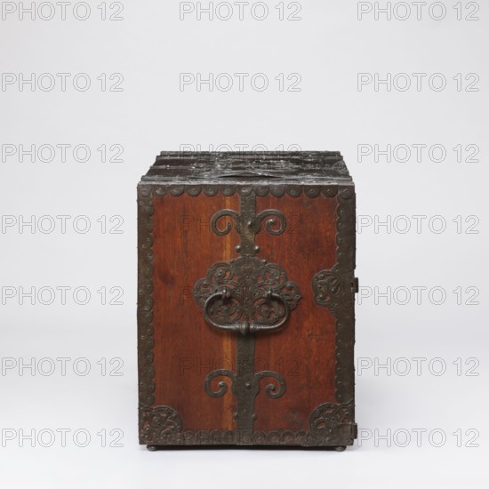 Cabinet, late 17th century, Northern Germany, or Poland, cabinet with a drawer at the top and double doors below, richly decorated with openwork engraved fittings with grotesque motifs. Door leaves veneered on the inside with rosewood and ebony in geometric arrangements, divided by inlaid bone veining, with figures in engraved bone signed Hippocrates on the left and Hermes on the right. Behind the doors are twelve compartments. Drawer and door locks fitted with engraved steel plates; the drawer lock blocks the left door leaf. Steel hinges. Motifs include grotesques, fantastic animals and figures, male figures, Hermes, plant tendrils, wickerwork ornament. Height 70.1 cm, width 89.2 cm, depth 55.9 cm., A wooden chest with a rectangular front face, showing a warm brown wood grain and darker brown to black metal hardware, including ornate decorative metal straps and corner plates with scalloped edges, an intricate central metal escutcheon with a looping handle, and additional metalwork alo...